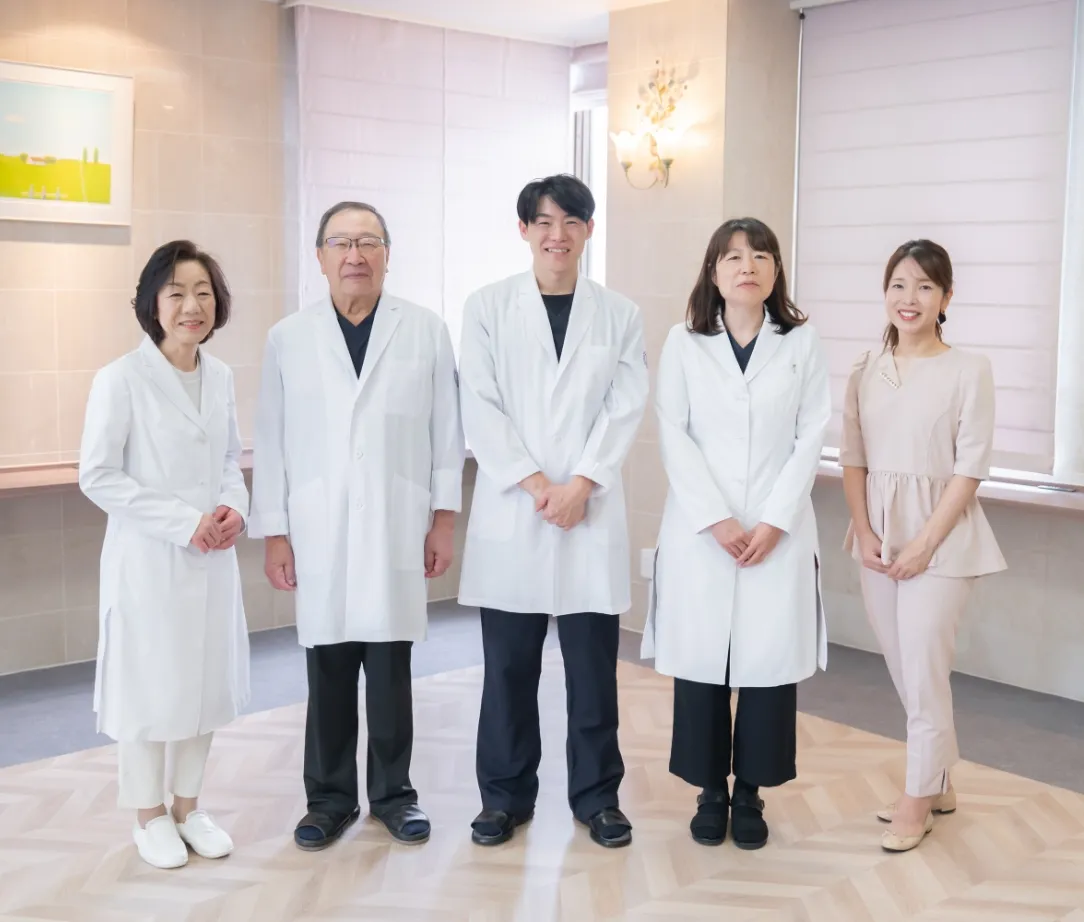 白衣を着た医療スタッフ4名と受付スタッフ1名が横一列に並んで微笑んでいる