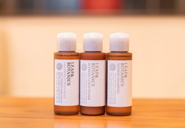 産院で提供されるアメニティグッズ、『LEAF & BOTANICS』シリーズのミニボトル。シャンプーやボディソープなど、茶色いボトルに入った3本が木製のテーブルの上に並べられている。